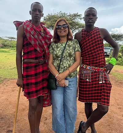 Kenya family safari cultural experience with a traveler posing alongside two Maasai men in traditional red shuka clothing in the African savanna