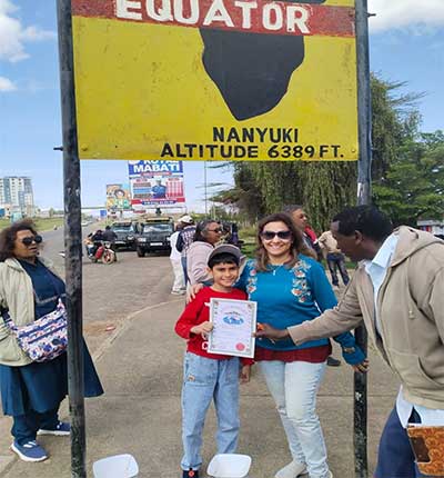 Family on a Kenya safari posing with a local guide and Equator certificate at the Nanyuki Equator landmark during a memorable family adventure.