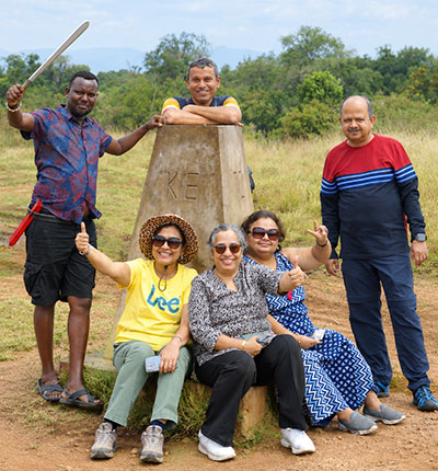 Family safari in Kenya with six travelers and a local guide posing beside a landmark in the African savanna during an unforgettable group adventure.