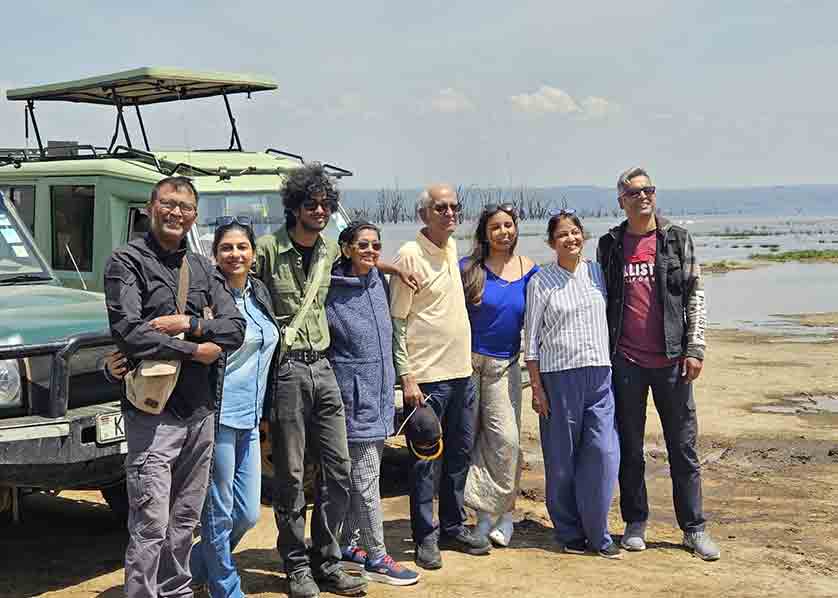 Family safari in Kenya with a group of travelers posing beside a safari vehicle against a scenic African landscape during a memorable wildlife adventure
