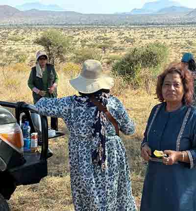 Three family safari travelers and one safari guide exploring the Kenyan savanna beside a safari vehicle during a memorable family wildlife adventure